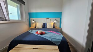 Un llit amb un capçal blau, dues làmpades de nit i una panxa de fusta en una habitació amb finestra.