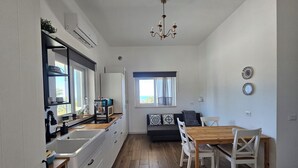 Una cuina moderna amb forn incorporat, zona de menjador amb taula i cadires de fusta, i vistes a l'exterior a través d'una finestra.