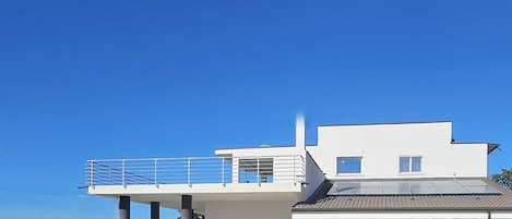 Una casa moderna de dos pisos con balcón, paneles solares y vista al mar.