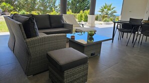 A patio area with a sofa, ottoman, and chairs, a glass-top coffee table, and a view of the outdoors.