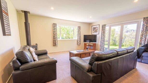 A living room with two leather sofas, a television, and a window with curtains. - Farrant Family Escape – Roomy Wanaka Retreat (Wānaka)