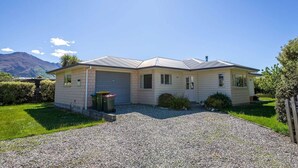 A single-story house with a garage, a gravel driveway, and a mountain in the background. - Farrant Family Escape – Roomy Wanaka Retreat (Wānaka)