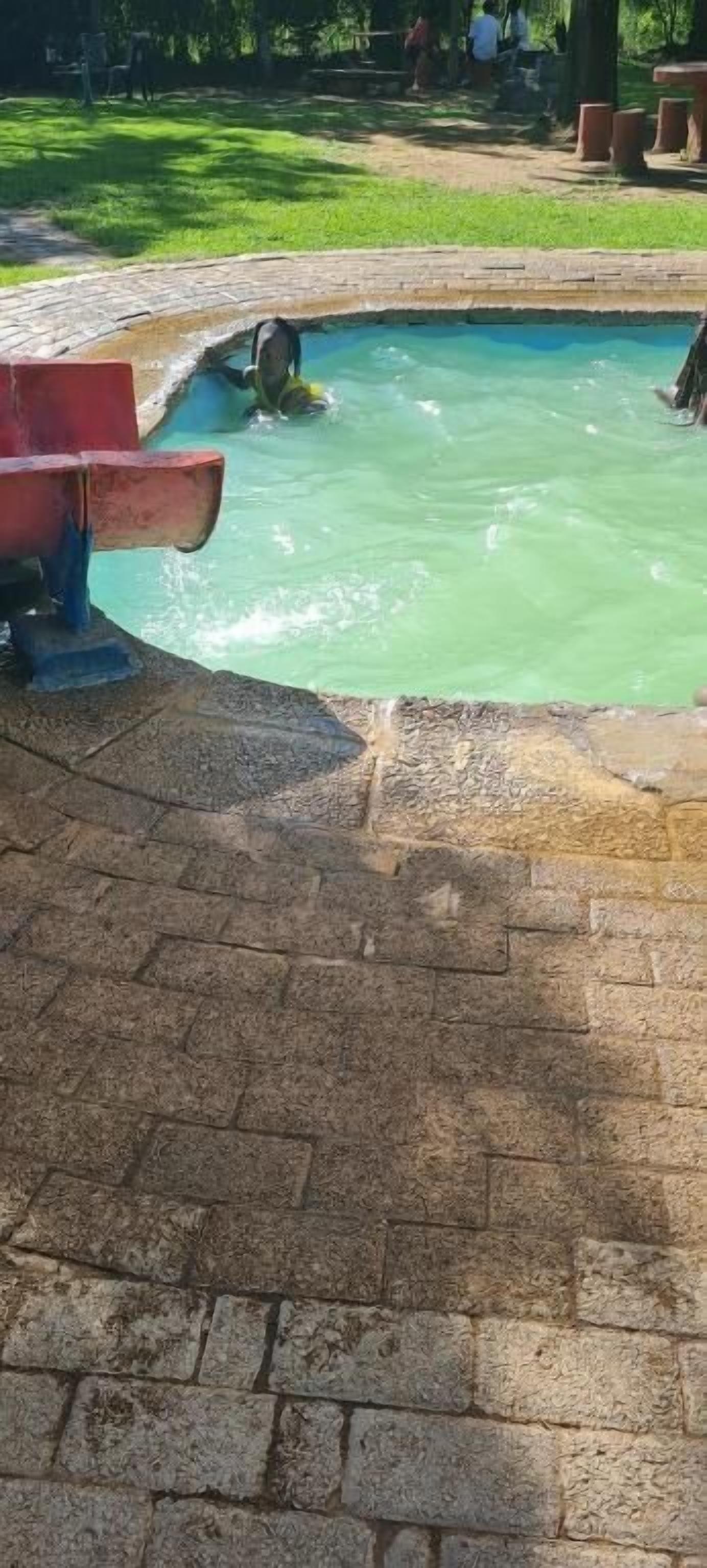 A swimming pool with a brick border and a grassy area in the background.