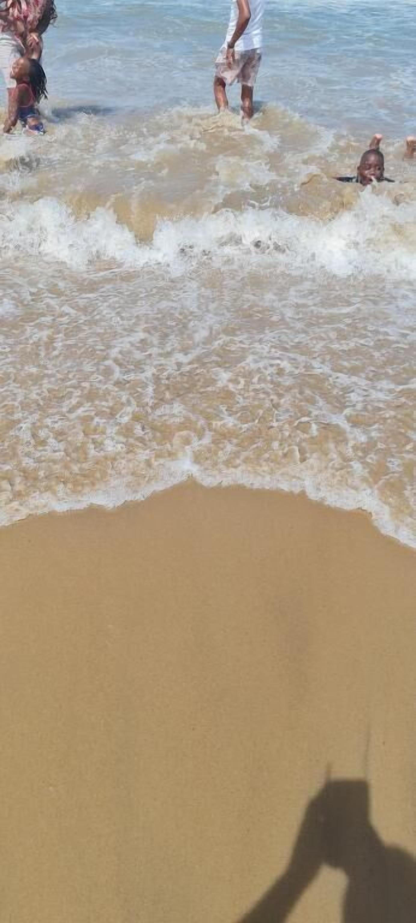 A beach with waves and people in the water.