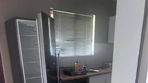 A compact kitchen with a refrigerator, washing machine, and a metal rack. - Room-yoxall Overnight Stays (Durban)
