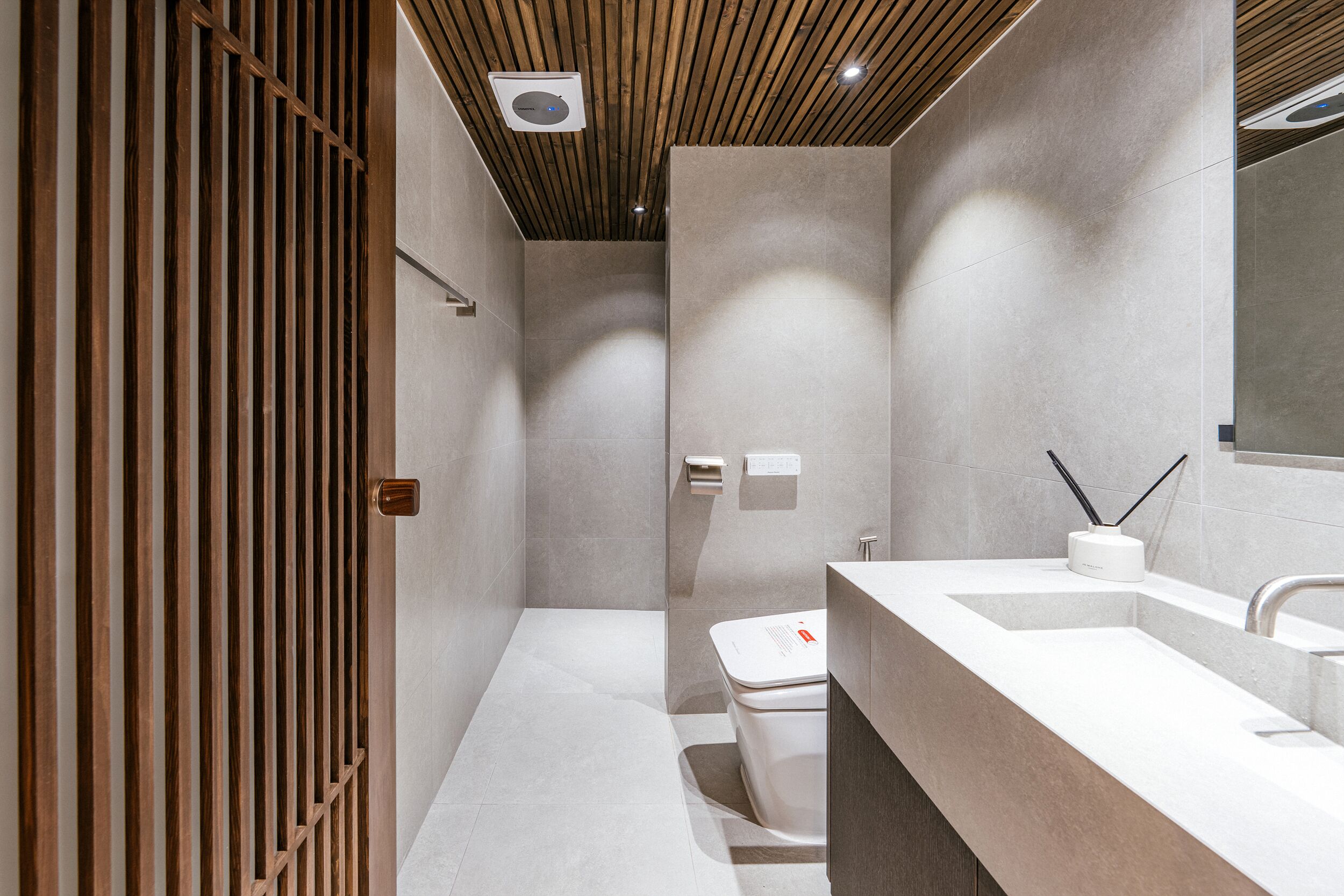 Un baño moderno con puerta de listones de madera, un inodoro, un lavabo y un espejo.