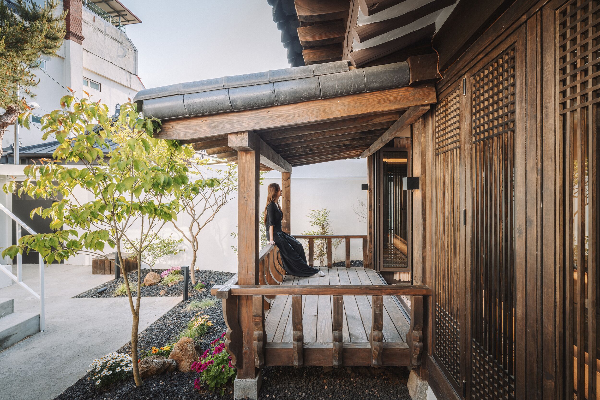 A wooden deck with a person sitting, surrounded by a garden with rocks and plants.