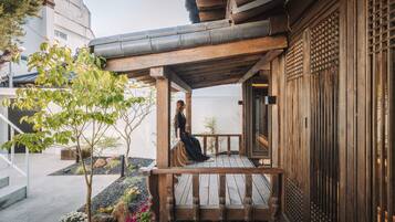 A wooden deck with a person sitting, surrounded by a garden with rocks and plants.