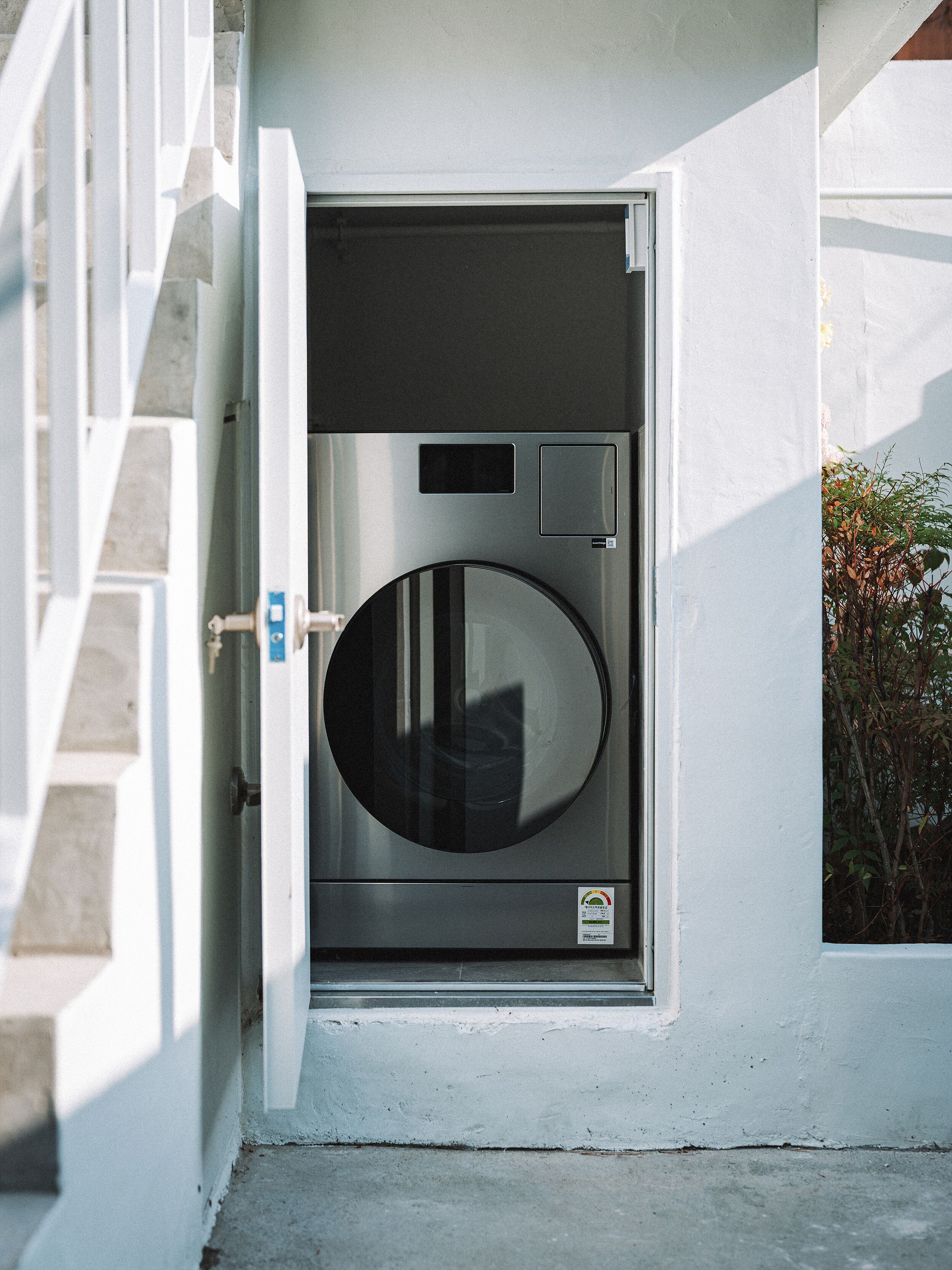 A compact, modern laundry room with a built-in washer and dryer, a small window, and a door with a handle.