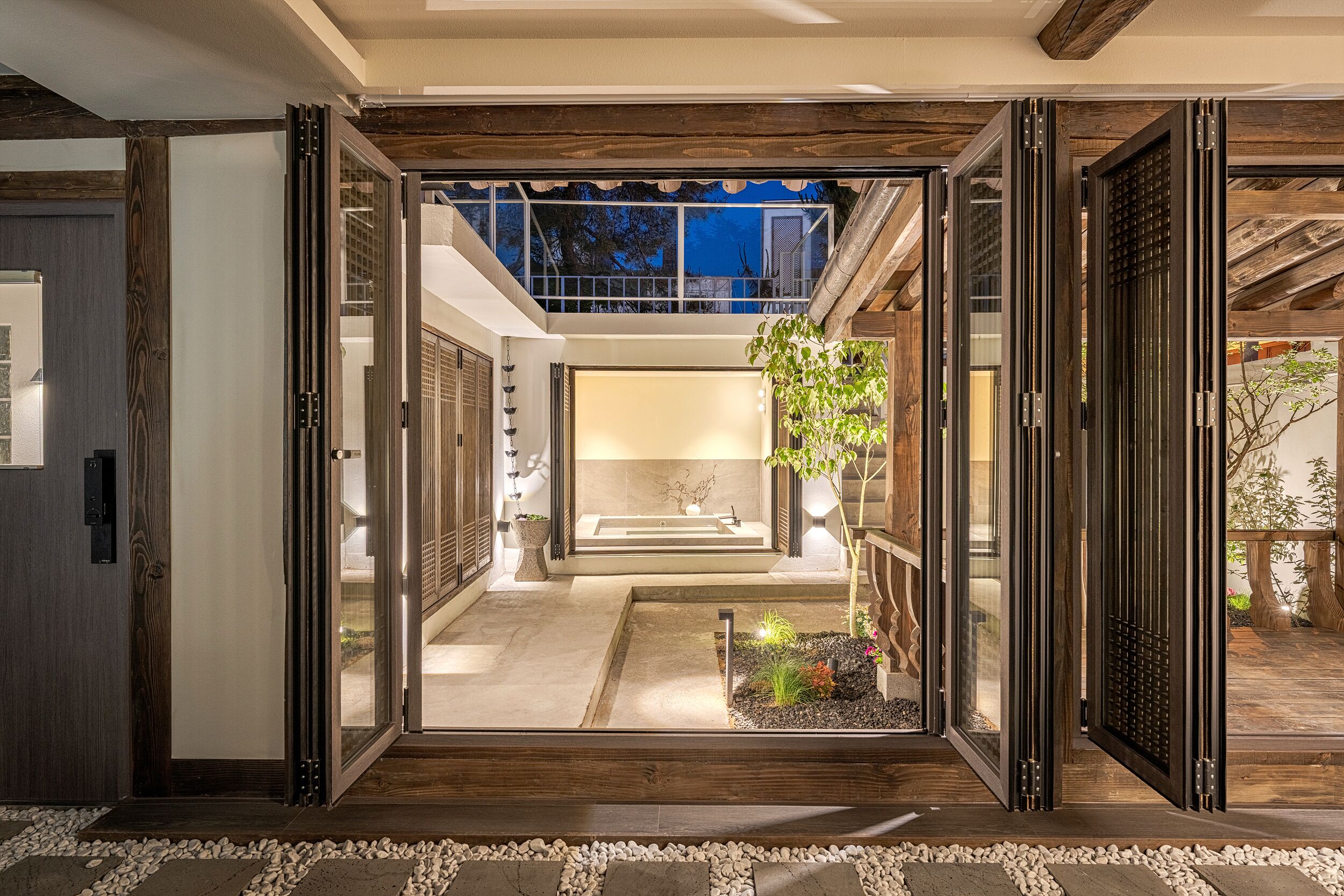 An open interior space with a view of a garden, a bathtub, and a staircase leading to a second floor.