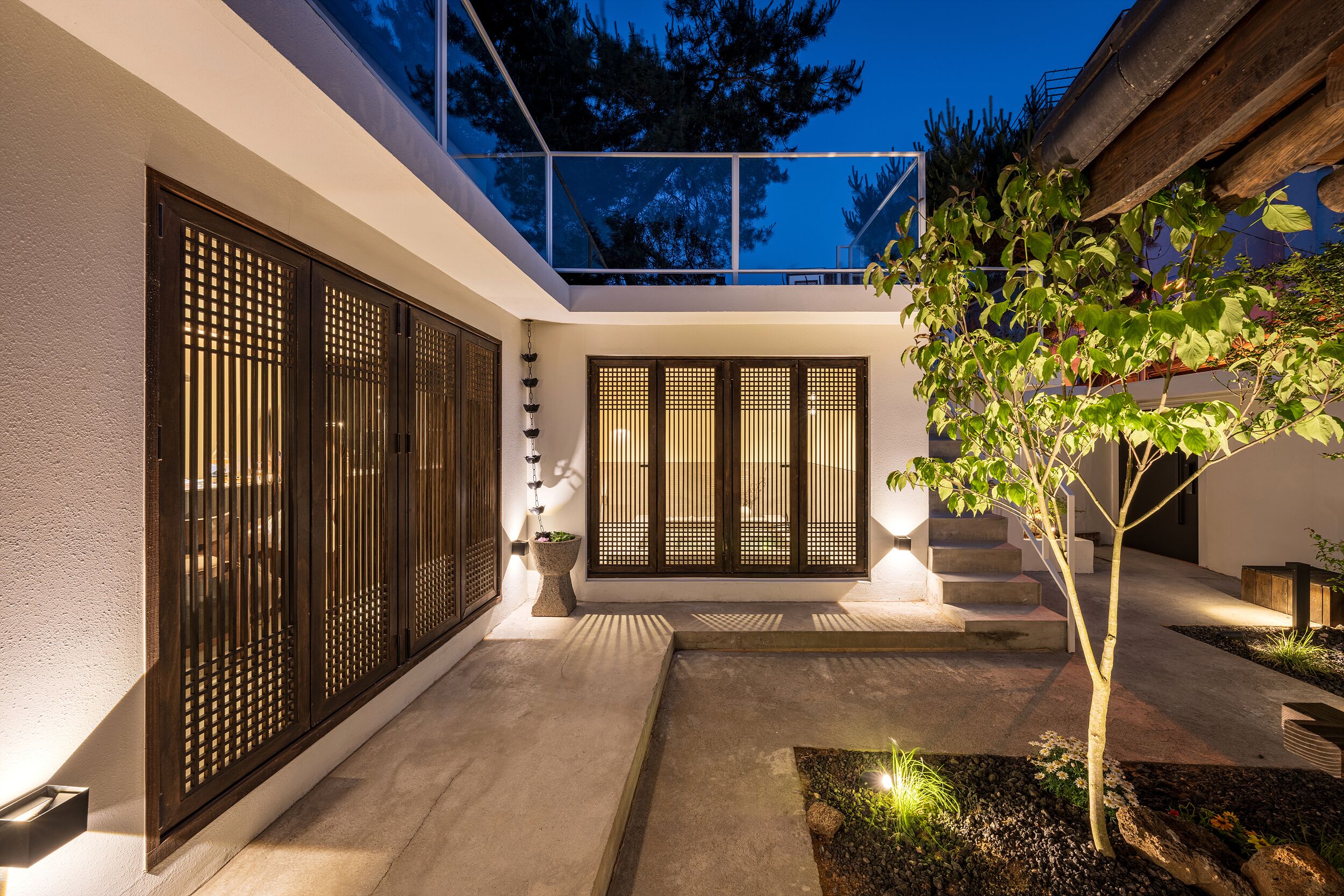 A modern building with a glass balcony, a wooden staircase, and a small garden area.