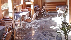 An outdoor patio with stone flooring, wooden furniture, and a stone wall.