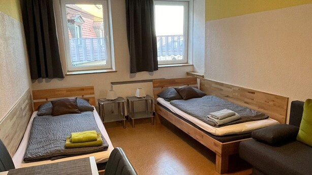 A compact room with two beds, a desk, a chair, and a sofa.
