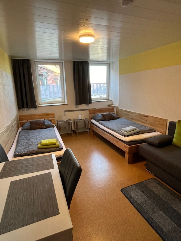 A compact room with two beds, a desk, a chair, and a sofa.