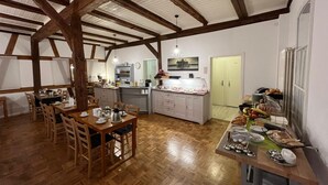 A spacious kitchen with wooden beams, a dining area with a wooden table and chairs, and a breakfast bar with various food items.