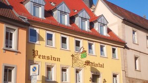 A building with a red-tiled roof, a sign reading 'Pension Malinal,' and a church spire in the background.