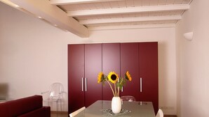 Ein Essbereich mit einem Glastisch, roten Stühlen, einer weißen Vase mit Sonnenblumen und einem roten Schrank.