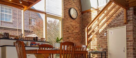 A kitchen with a wooden table, chairs, a clock, and a brick wall.