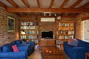 A living room with a brick wall, wooden bookshelves, a television, and blue patterned sofas.