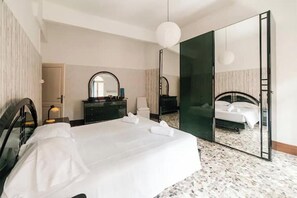 Une chambre d’hôtel avec un grand lit, un miroir, une commode et une porte donnant sur une autre pièce.