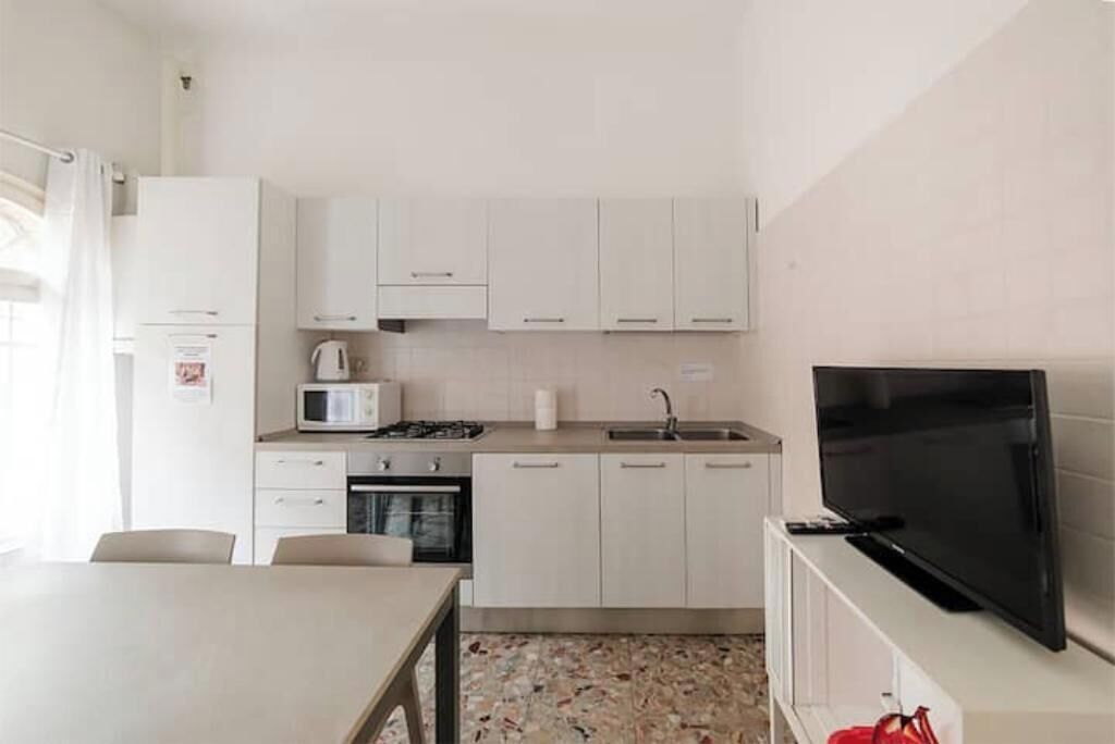 Une cuisine compacte avec des meubles blancs, un four à micro-ondes, une cuisinière et un téléviseur.
