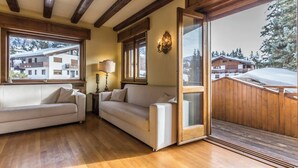 Un'accogliente stanza con soffitto in legno, un divano, una lampada e una porta scorrevole in vetro che dà su un balcone.