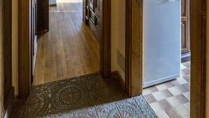 Un corridoio con pareti in legno e pavimento piastrellato che conduce a una zona cucina con frigorifero e bollitore.