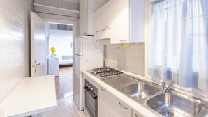 Une cuisine moderne avec des meubles blancs, un évier en acier inoxydable et une fenêtre ornée de rideaux légers.