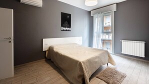 A bedroom with a bed, a radiator, a window with curtains, a hanging light fixture, and a wall-mounted air conditioner. - Mascarella (Bologna)