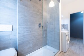Une salle de bain moderne avec une douche à parois de verre, des toilettes et un lave-linge.