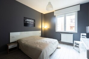 Une chambre à coucher avec un lit, une table de chevet, une lampe, une fenêtre et un tableau au mur.