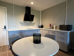 A compact kitchen with a round table, a microwave, a sink, and a TV mounted on the wall. - G-Kroen (Eidskog)