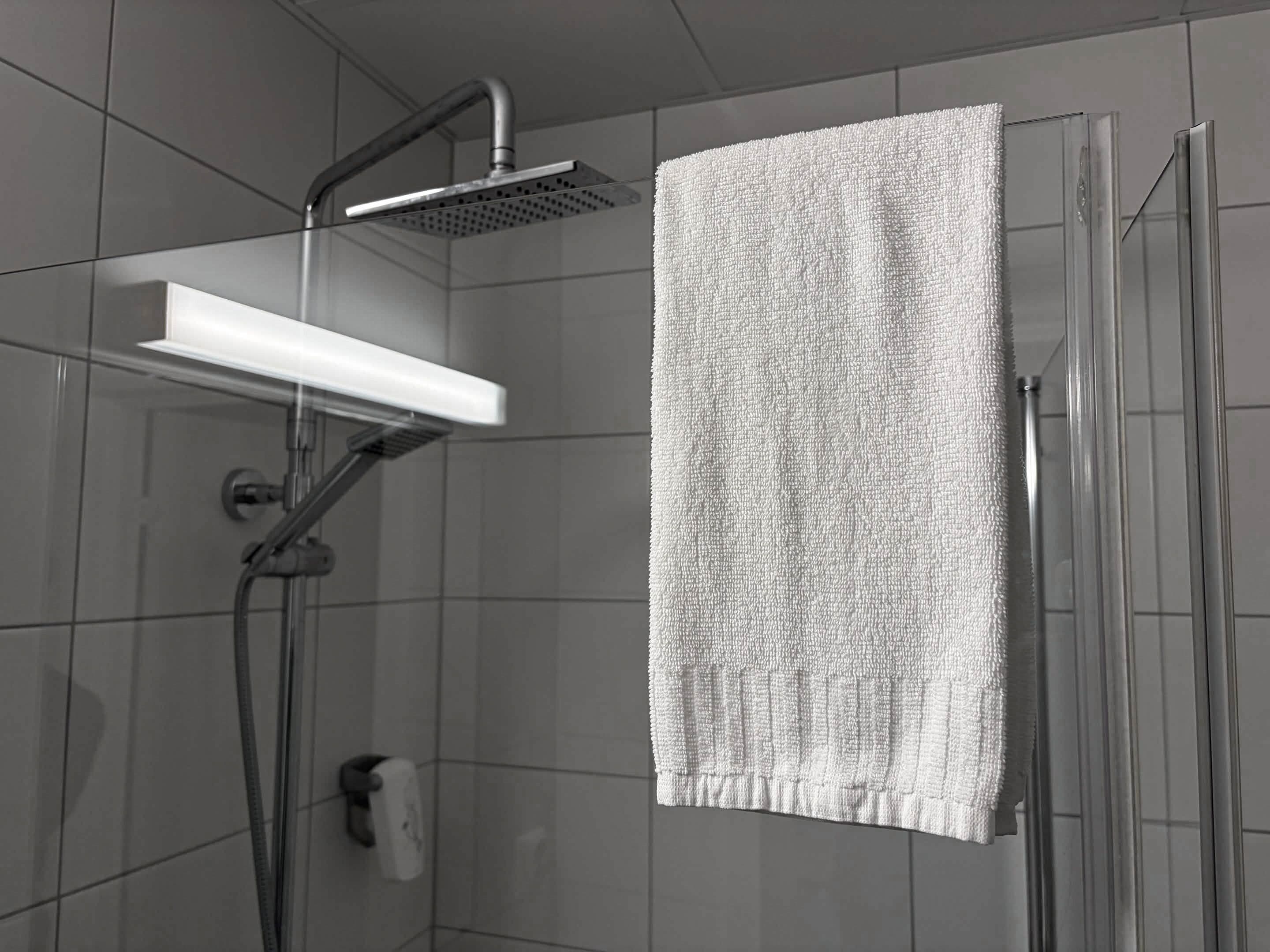 A shower with a handheld showerhead and a towel rack with a towel.