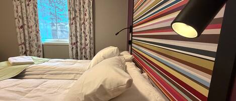 A hotel room with a bed, a window with curtains, and a colorful striped wall.