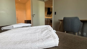 Una habitación de hotel con una cama, una silla y un baño visible a través de una puerta abierta.