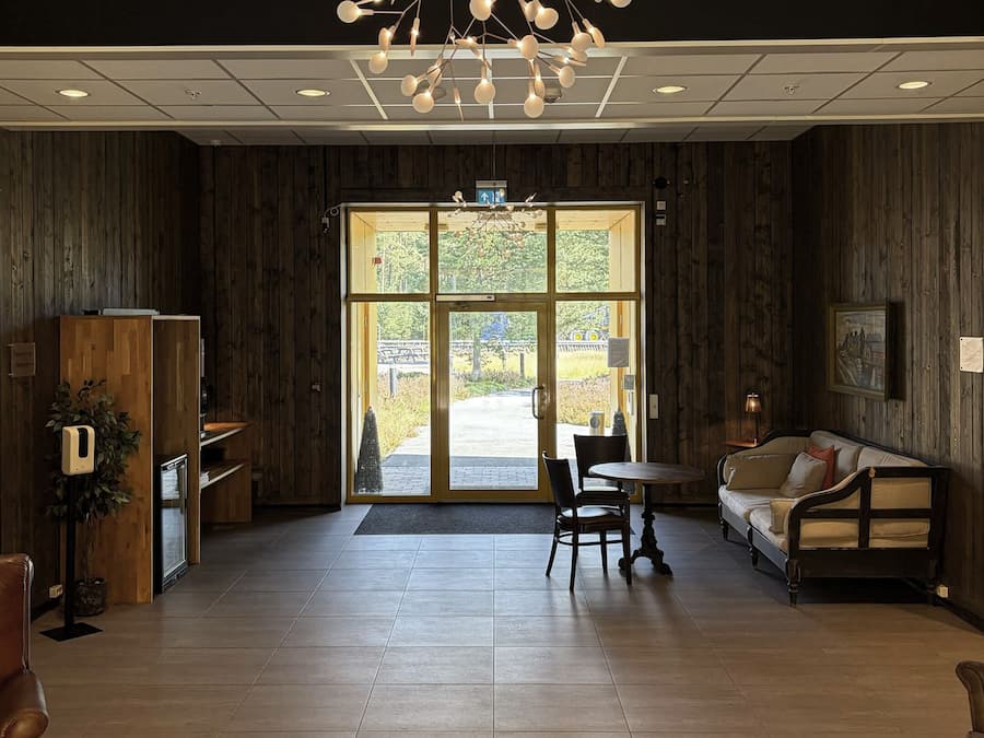 A reception area with a wooden interior, a seating area with a sofa and chairs, and a large glass door leading outside.