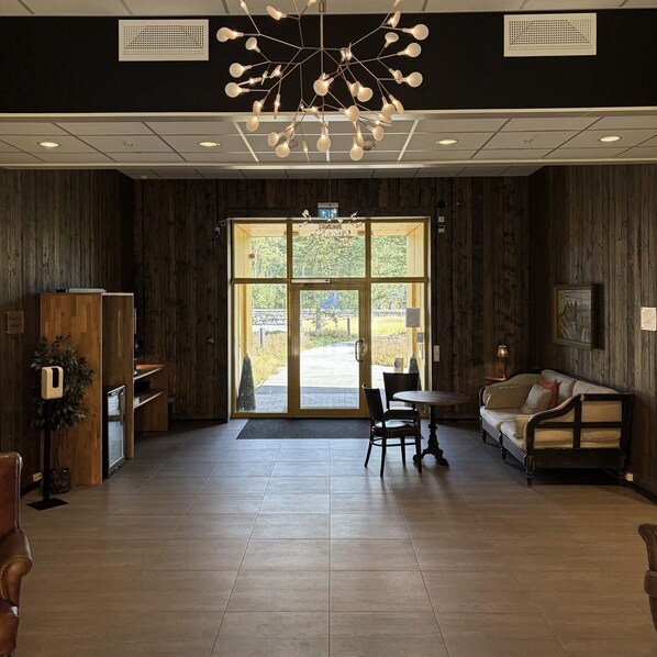 A reception area with a wooden interior, a seating area with a sofa and chairs, and a large glass door leading outside.