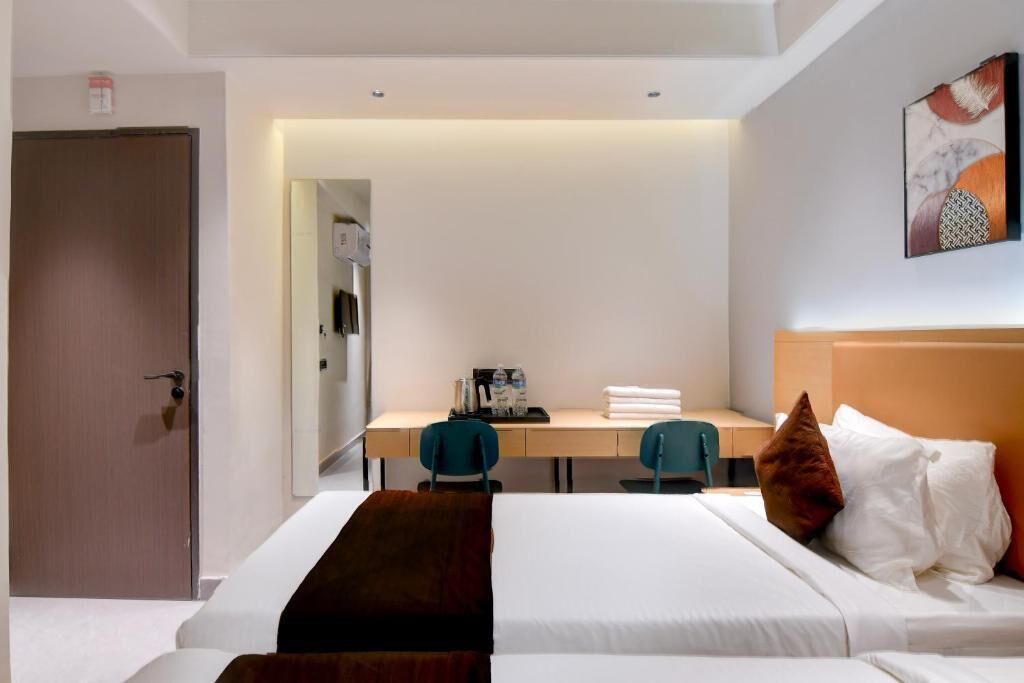 A hotel room with a bed, a desk, two chairs, a door, and a painting on the wall.