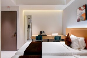 A hotel room with a bed, a desk, two chairs, a door, and a painting on the wall.
