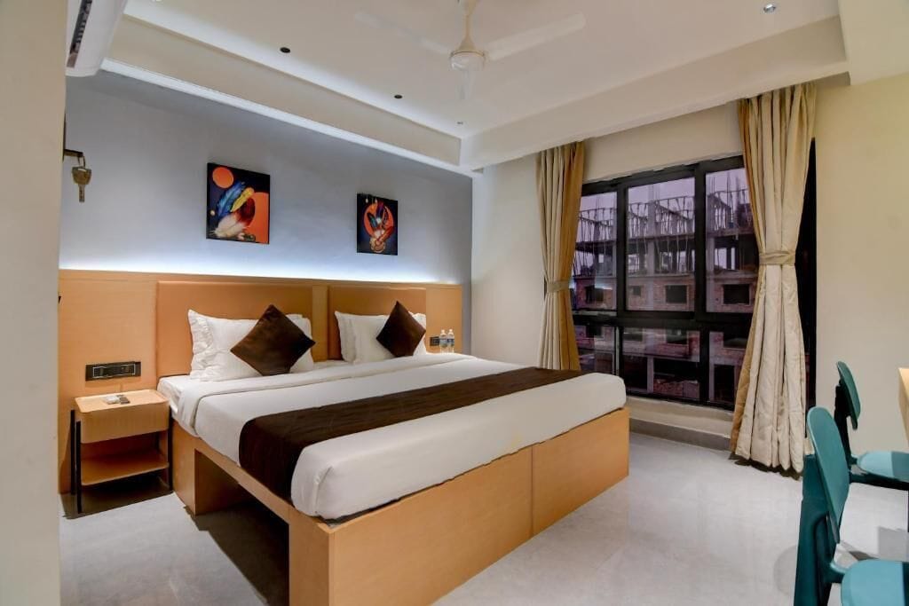 A hotel room with a large bed, a nightstand, a desk with a chair, and a window with curtains.