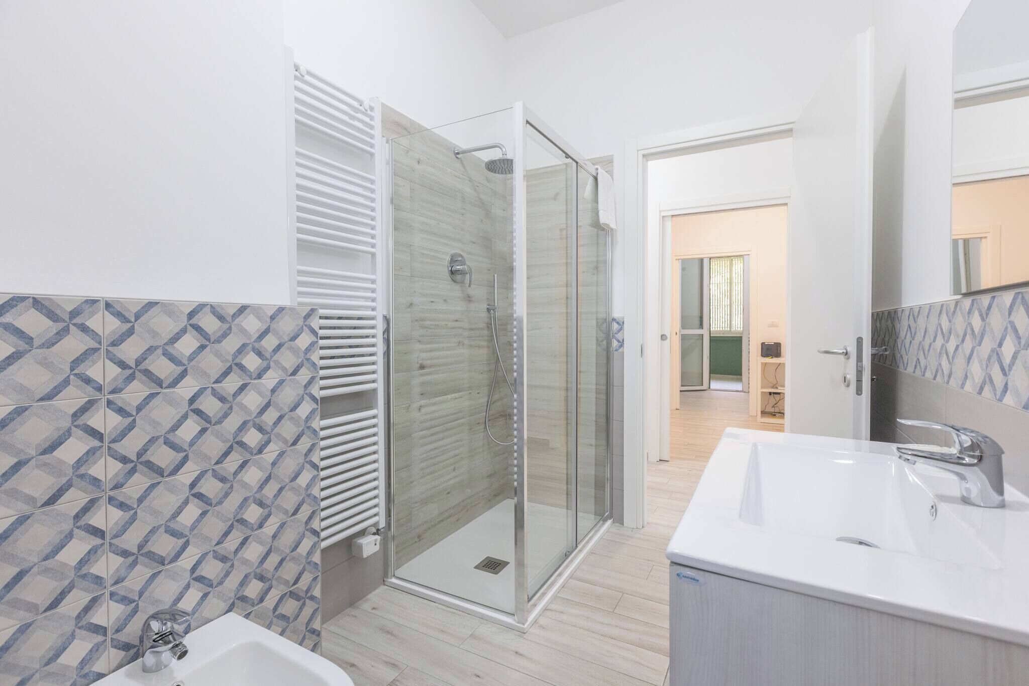 A modern bathroom with a glass shower enclosure, a white sink, and patterned tiles.