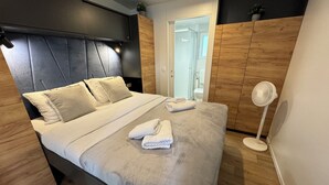 A modern bedroom with a bed, wooden headboard, a bedside fan, and a view of a bathroom. - Mobile Home Saky, Camp Soline (Biograd na Moru)