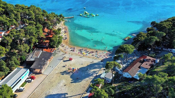 An aerial view of a beach with clear waters, a small dock, and a building with a sign that reads 'DUBAI.' - Mobile Home Saky, Camp Soline (Biograd na Moru)
