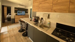 A modern kitchen with a built-in stove, a sink, and bar stools. There is a television in the background, and wooden cabinets above the counter. - Mobile Home Saky, Camp Soline (Biograd na Moru)