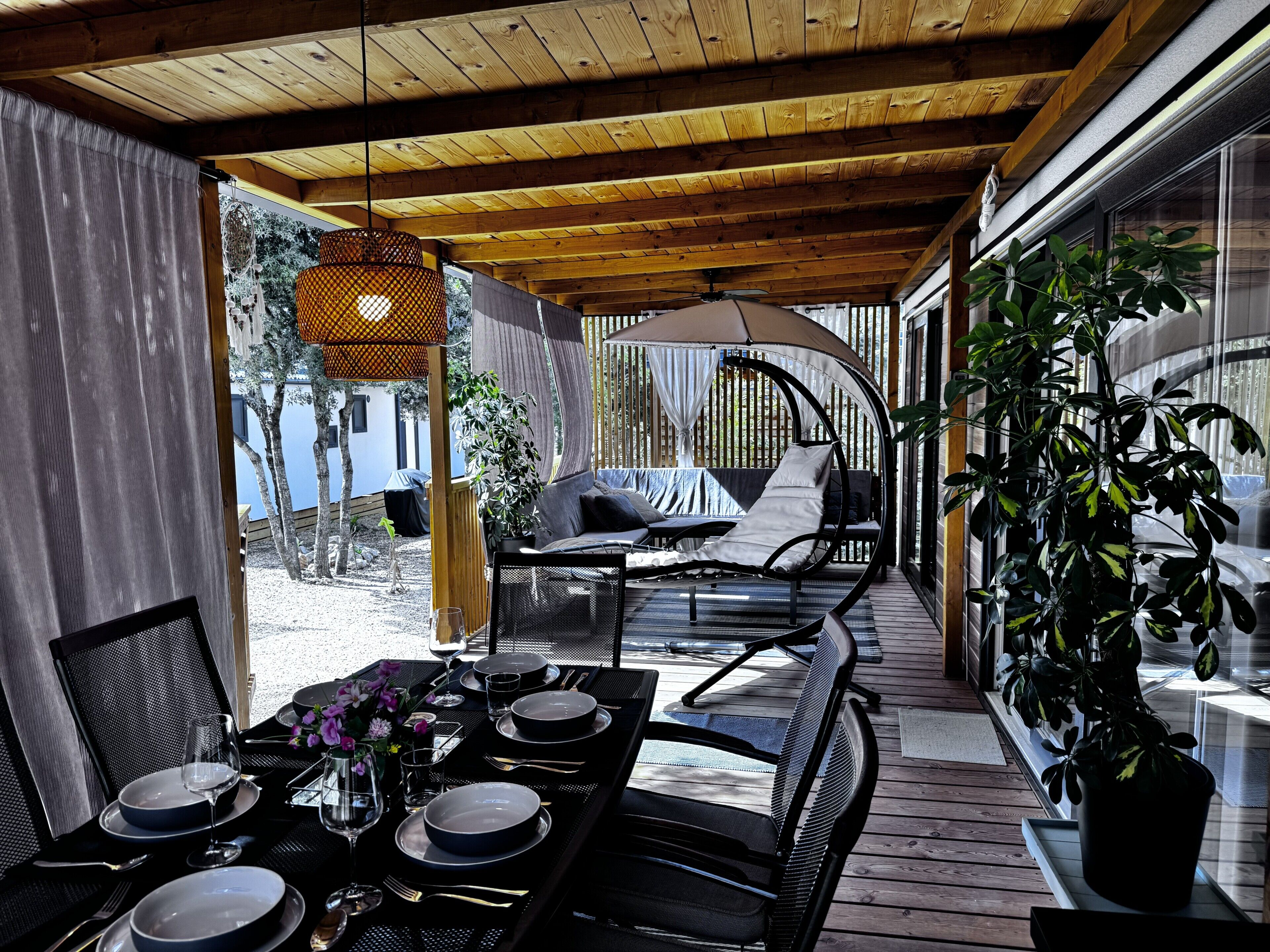 Une terrasse extérieure avec une table à manger pour quatre personnes, un coin salon avec des coussins et une plante en pot.