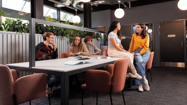 Un espace de bureau moderne avec une grande table, plusieurs chaises et un groupe de personnes engagées dans une discussion.