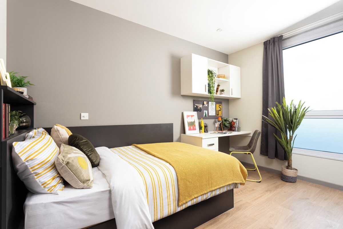A modern bedroom with a bed, desk, and potted plant.