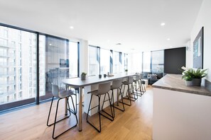 A modern kitchen with a long counter, bar stools, and large windows offering city views. - Student Only Arch View House (Wembley)