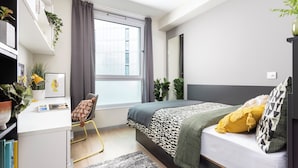 Une chambre moderne avec un lit, un bureau, une chaise et une grande fenêtre.