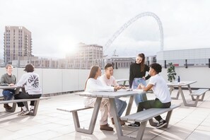 A rooftop terrace with outdoor seating, a Ferris wheel in the background, and modern buildings. - Student Only Arch View House (Wembley)